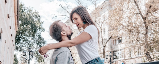 Una felice coppia di innamorati si guarda negli occhi per la strada della città Una giovane donna abbraccia un uomo mettendogli le mani sulle spalle