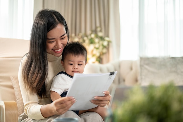 Una felice donna d'affari asiatica si concentra sulla lettura di documenti e sulla cura del suo piccolo figlio.