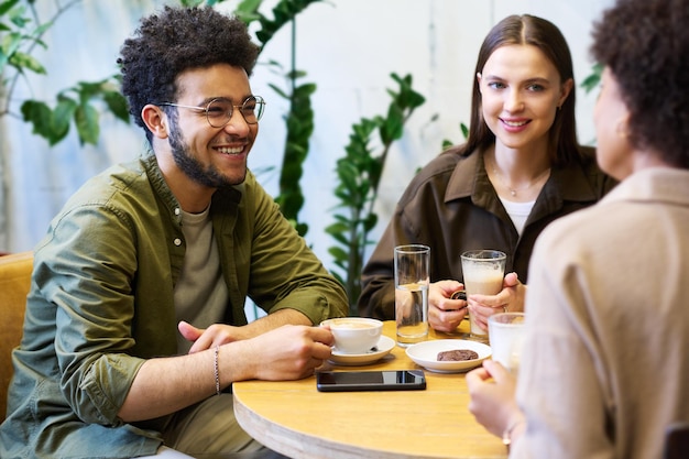 Una felice giovane coppia interculturale che beve caffè e ascolta un amico