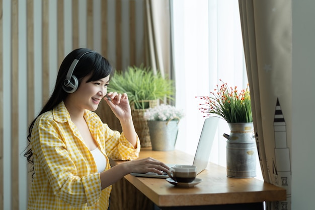 Una felice studentessa asiatica indossa un auricolare per studiare il corso online e comunica tramite videochiamata in conferenza, utilizzando un computer portatile