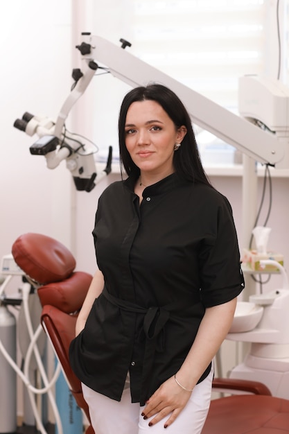 Una femmina di dentista in uniforme pone su uno sfondo di apparecchiature odontoiatriche in uno studio dentistico.