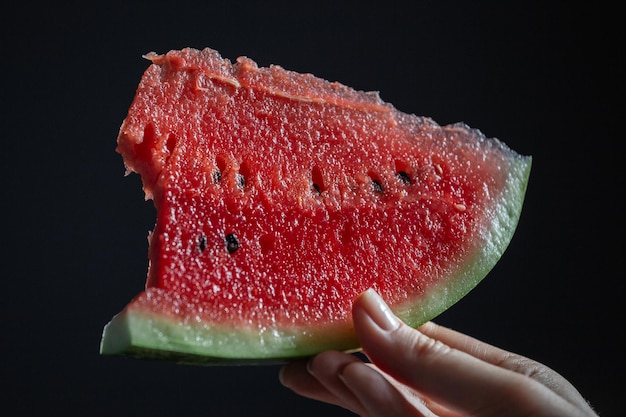 Una fetta di cocomero in mano su uno sfondo scuro Una fetta di cocomero