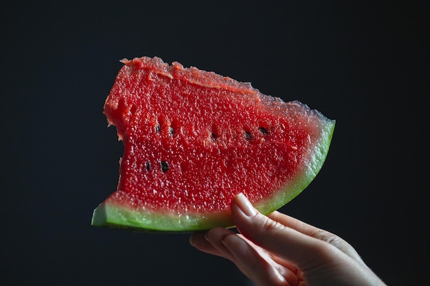 Una fetta di cocomero in mano su uno sfondo scuro Una fetta di cocomero