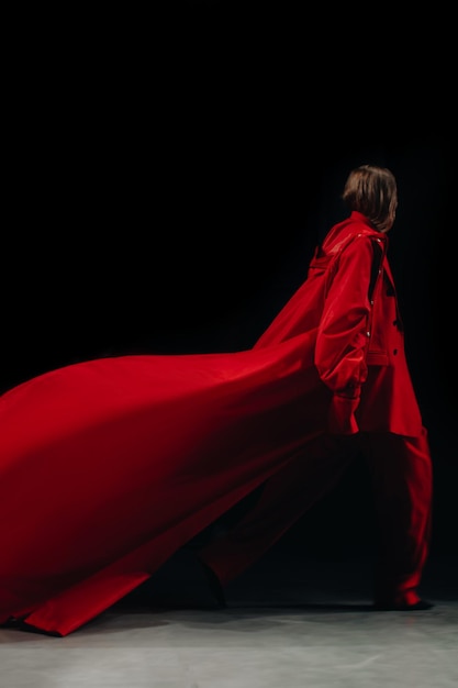 Una figura femminile vestita con un vestito rosso creativo, pantaloni e giacca che cammina sulla passerella