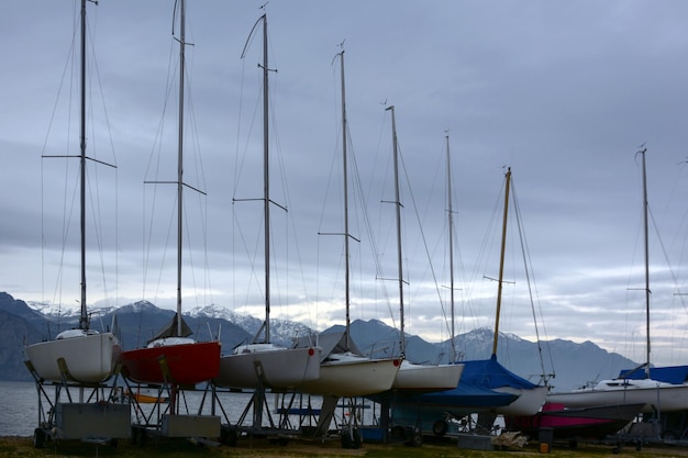 Una fila di barche a vela sulla riva è immagazzinata su piattaforme sullo sfondo delle montagne