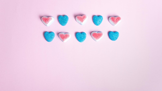 Una fila di caramelle a forma di cuore rosa e blu su sfondo rosa.