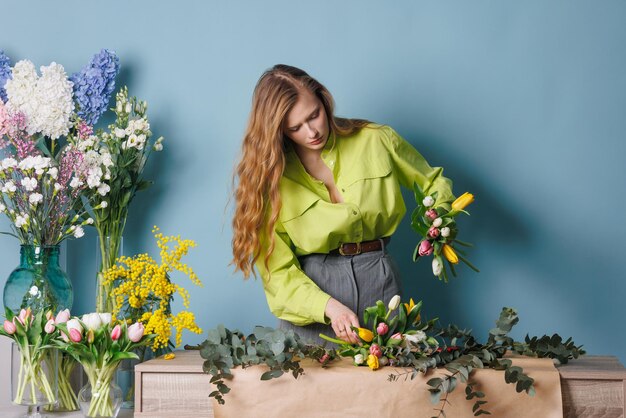 una fiorista raccoglie un bouquet di fiori di tulipano di primavera su uno sfondo blu pulito