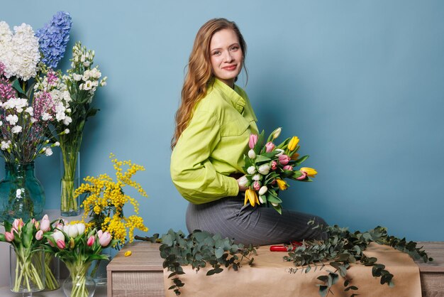 una fiorista raccoglie un bouquet di fiori di tulipano di primavera su uno sfondo blu pulito