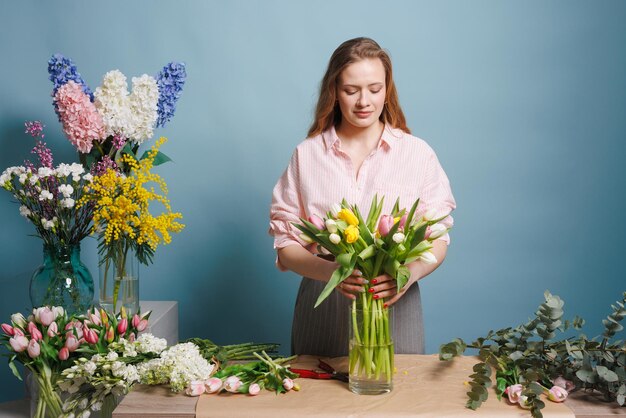 una fiorista raccoglie un bouquet di fiori di tulipano di primavera su uno sfondo blu pulito