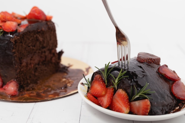 Una forchetta inossidabile che raccoglie un pezzo di deliziosa torta al cioccolato con fragole su sfondo bianco per il concetto di cibo e prodotti da forno