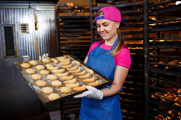 Una fornaia professionista tiene in mano un vassoio con biscotti freschi. Dolci in una pasticceria