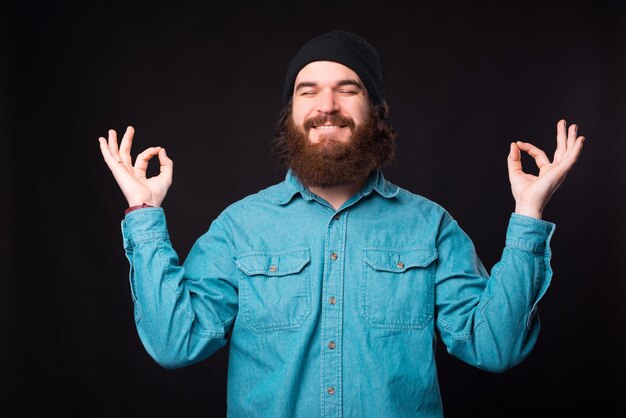 Una foto di un uomo rilassato seduto in una posizione zen sorridente vicino a un muro scuro