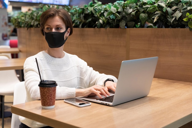 Una foto di una giovane donna con una maschera protettiva che siede presso la food court di un centro commerciale