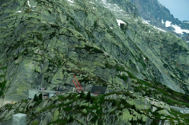 Una foto di una montagna verde e rocciosa con vista sulla casa al Passo del Grimsel