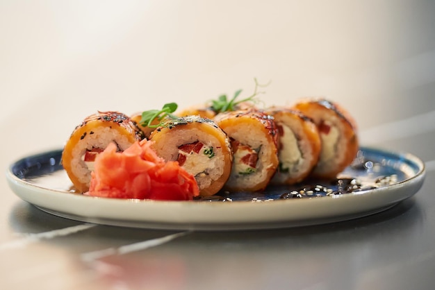 Una foto in primo piano di involtini di sushi freschi con salmone philadelphia e tonno su un piatto di ceramica blu con salsa di sesamo wasabi e foglie tavolo in pietra nera