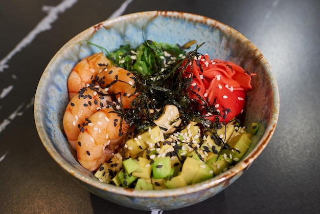 Una foto in primo piano di un poke bowl con alga Chuka Wakame wasabi avocado anacardi nori e gamberetti su un tavolo di pietra nera