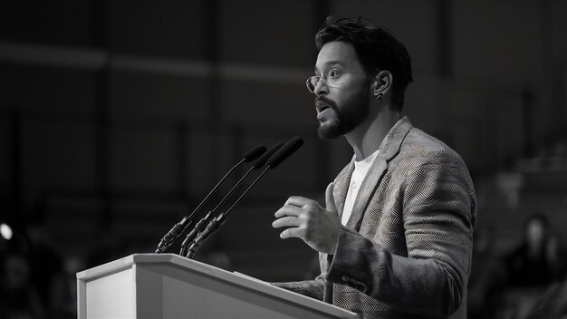 Una foto in scala di grigio di un maschio che parla sul podio