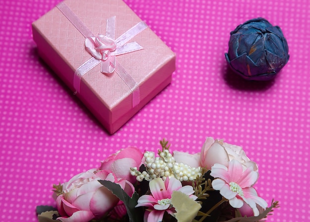 Una foto piatta di un mazzo di fiori un regalo sotto forma di scatola e accessori su un rosa