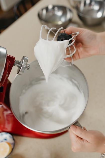 Una foto ravvicinata della mano di una donna che mostra la meringa con la frusta vicino a una ciotola di acciaio inossidabile in una cucina