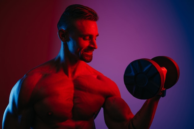 Una foto ravvicinata di un uomo muscoloso con la barba che sta facendo riccioli per bicipiti con manubri sotto luci blu e rosse