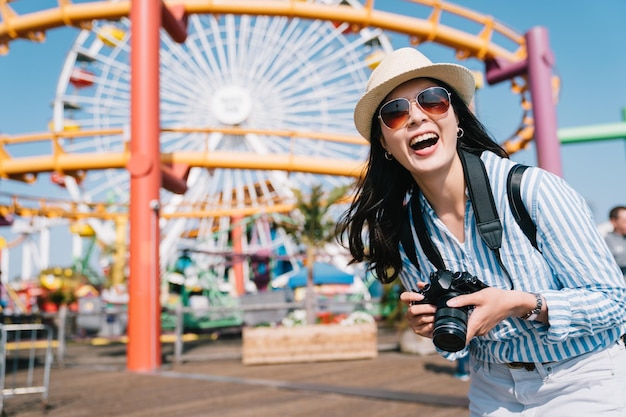 una fotografa allegra in piedi nel parco divertimenti e con in mano la sua macchina fotografica