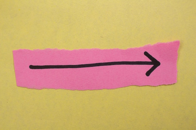 Una freccia rosa è disegnata su un pezzo di carta rosa con una freccia nera che punta a sinistra.
