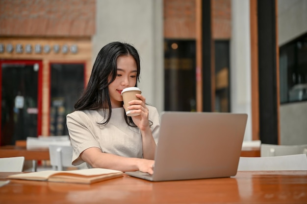 Una freelance asiatica sta sorseggiando un caffè e lavorando a distanza in un bar