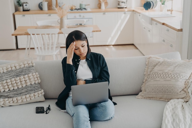 Una freelance femminile perplessa lavora su laptop risolvendo problemi seduti sul divano a casa Lavoro a distanza