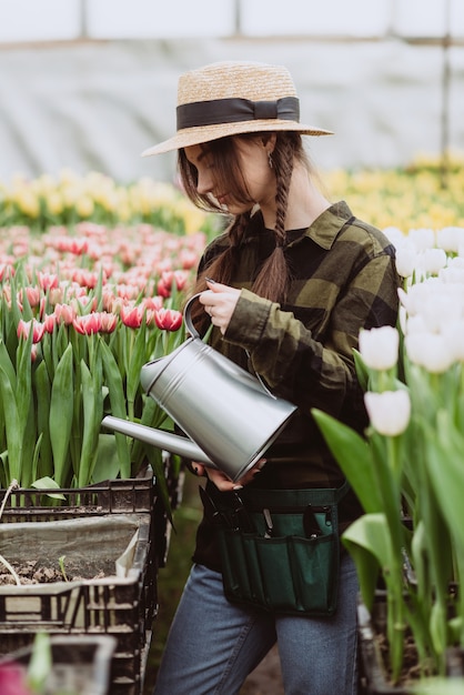 Una giardiniera con cappello e guanti innaffia un'aiuola di tulipani usando un annaffiatoio