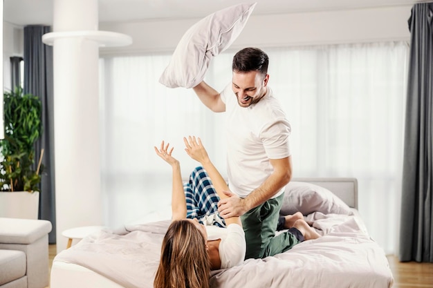 Una giocosa coppia mattutina che litiga con i cuscini a letto nel loro appartamento