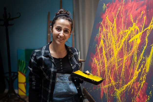 Una giovane artista di talento sorridente è in piedi accanto a un cavalletto con una tela su cui ha dipinto