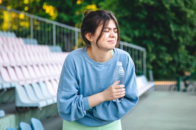 Una giovane atleta femminile che beve acqua dopo aver allenato il dolore al fianco