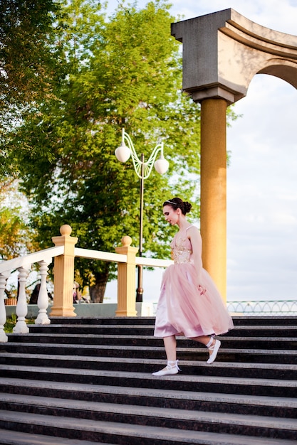 Una giovane ballerina in un abito di seta rosa scende con grazia i gradini in un arco con colonne sul...