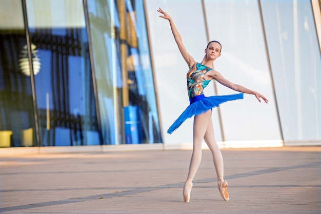 Una giovane ballerina in un tutù blu brillante sta ballando sullo sfondo di un paesaggio urbano