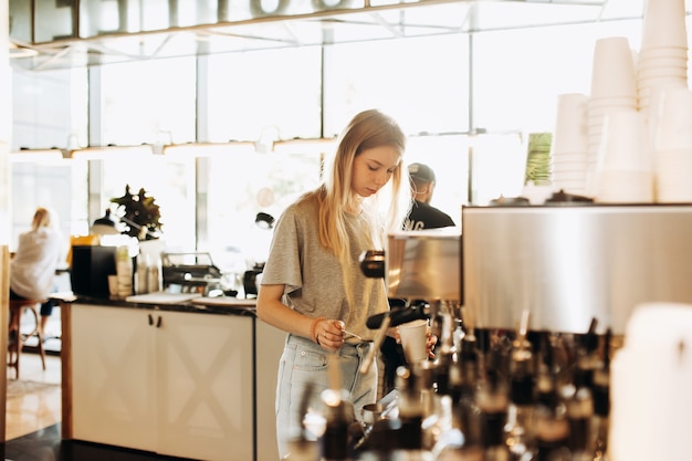 Una giovane bella bionda magra, vestita in modo casual, sta cucinando il caffè in una famosa caffetteria. .