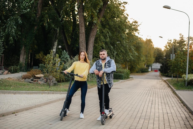 Una giovane bella coppia guida scooter elettrici nel parco in una calda giornata autunnale. Hobby e svago.
