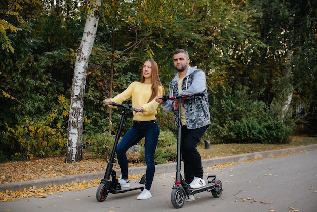 Una giovane bella coppia guida scooter elettrici nel parco in una calda giornata autunnale. Hobby e svago.