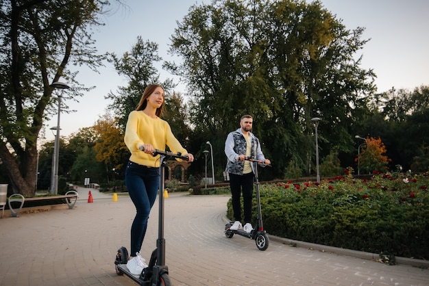 Una giovane bella coppia guida scooter elettrici nel parco in una calda giornata autunnale