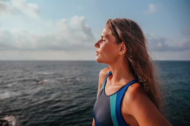 Una giovane bella donna abbronzata con i capelli lunghi in bikini blu si trova sulla roccia vicino al verde blu chiaro