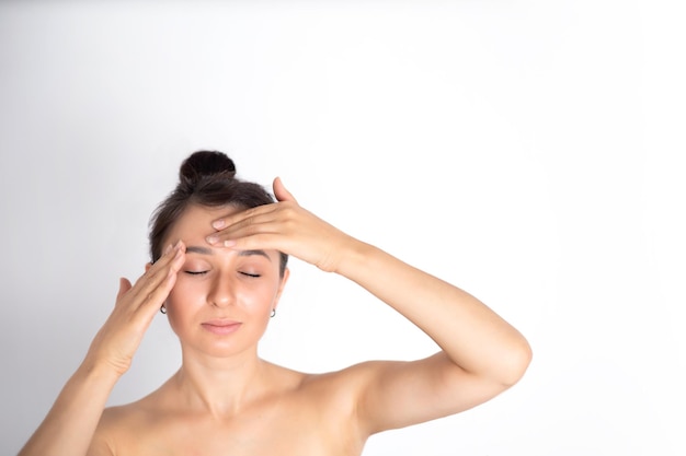Una giovane bella donna bruna massaggia il viso e il collo La naturalezza della cura di sé Posto di sfondo bianco per il testo