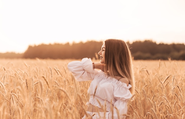 Una giovane bella donna cammina attraverso un campo di grano in abiti bianchi