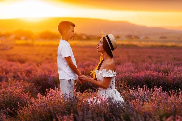 Una giovane bella donna con il suo giovane figlio sta camminando attraverso un bellissimo campo di lavanda e si gode il profumo dei fiori. Riposo e bella natura. Unità con la natura e armonia.