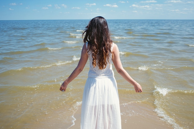 Una giovane bella donna in abito bianco cammina sulla spiaggia