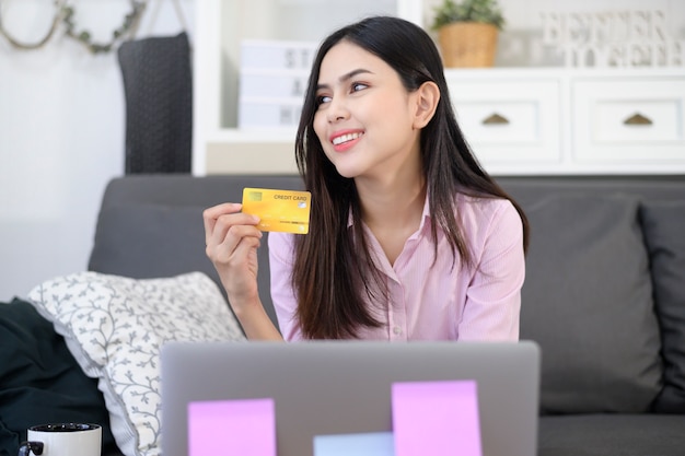 Una giovane bella donna sta utilizzando la carta di credito per lo shopping online sul sito Internet a casa, concetto di e-commerce
