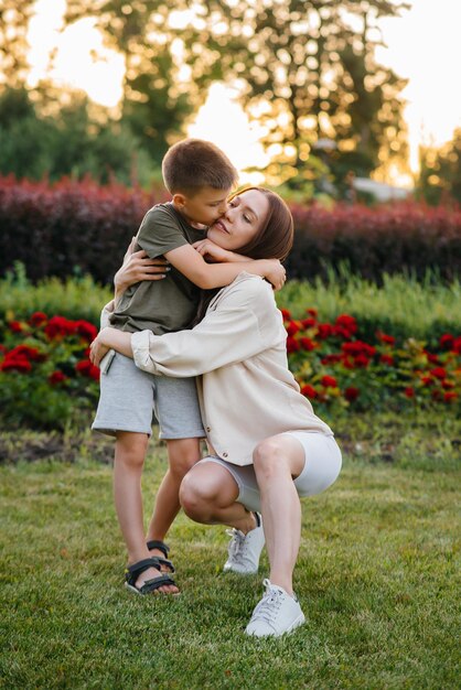 Una giovane bella madre bacia e abbraccia il suo piccolo figlio durante il tramonto nel parco. Famiglia felice a piedi nel parco.