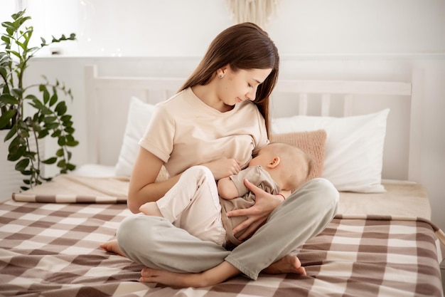 Una giovane bella madre con un bambino che si abbraccia sul letto a casa in camera da letto mamma allatta il bambino corretto allattamento al seno sano dei bambini