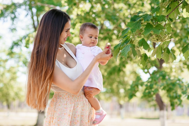 Una giovane bella madre con una figlia piccola nelle mani a piedi nel parco. Un bambino allegro sta giocando con le foglie su un albero.