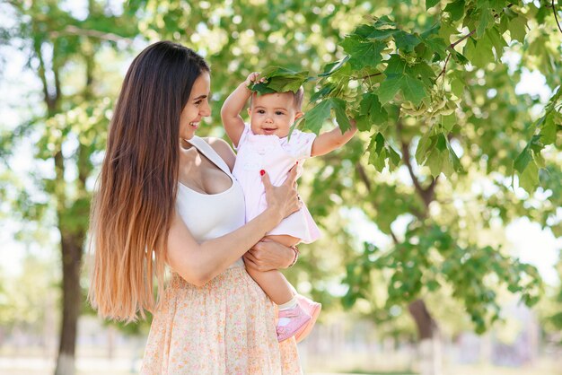 Una giovane bella madre con una figlia piccola nelle mani a piedi nel parco.