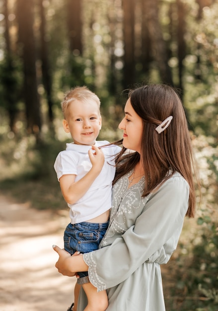 Una giovane bella madre tiene in braccio il suo giovane figlio e gioca con lui in estate nella natura.