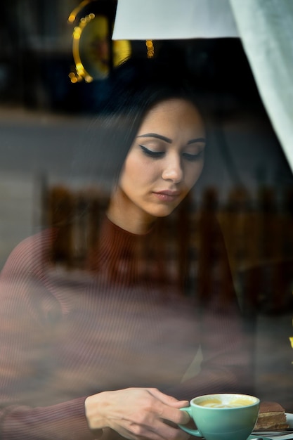 Una giovane bella ragazza a un tavolo in un caffè Vista attraverso la finestra